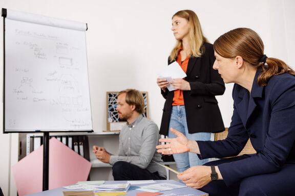 Zwei weibliche und eine männliche Person schaue auf ein Flipchart und unterhalten sich.