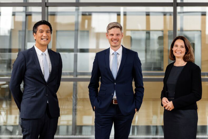 Die Rektoratsbeauftragten für Nachhaltigkeit: Professor Aaron Praktiknjo, Professor Niklas von der Aßen, Professorin Kathrin Greiff vor einer Glaswand.  Professor Praktiknjo in blauem Anzug mit weißem Hemd und hellblauer Krawatte, Professor von der Aßen in blauem Anzug mit weißem Hemd und hellblauer Krawatte, Professorin Greiff in dunkelblauem Etuikleid und schwarzem Blazer.  Sie lächeln in die Kamera.