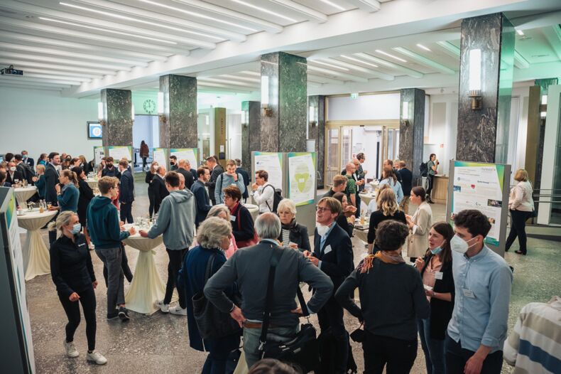 Das Bild zeigt die Auftaktveranstaltung der Initiative Humboldt N. Viele Menschen stehen in einer großen Halle und sprechen miteinander. Im Raum verteilt sind Plakate.