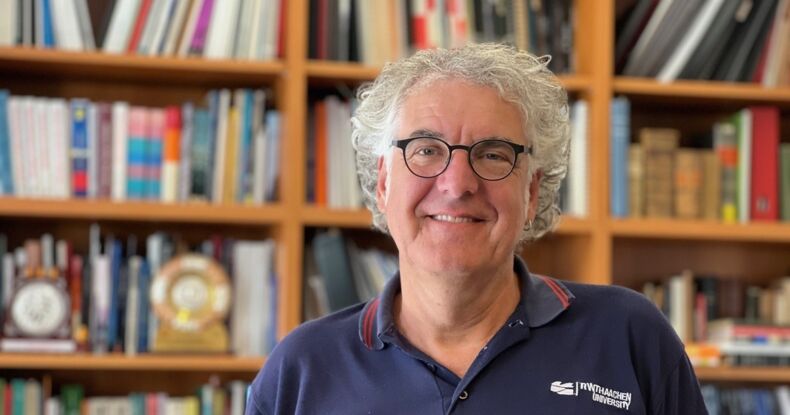 Das Bild zeigt Herrn Professor Doktor Reicherter. Er trägt ein blaues Hemd mit der Aufschrift RWTH Aachen University. Im Hintergrund ist ein Bücherregal zu sehen.