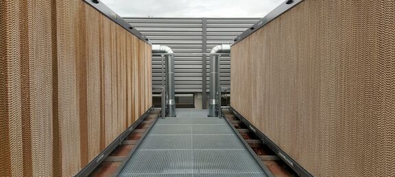 The photo shows a construction on the right and left side of a grating run. At the end, two pipes lead into the recooling unit, one on the right and one on the left. The cooling unit itself is visible from the outside with a fluted structure in light brown.