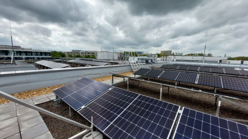 Das Bild zeigt mehrere Reihen von Solarpanelen auf einem Dach. Im Hintergrund ist ein bewölkter Himmel abgebildet.