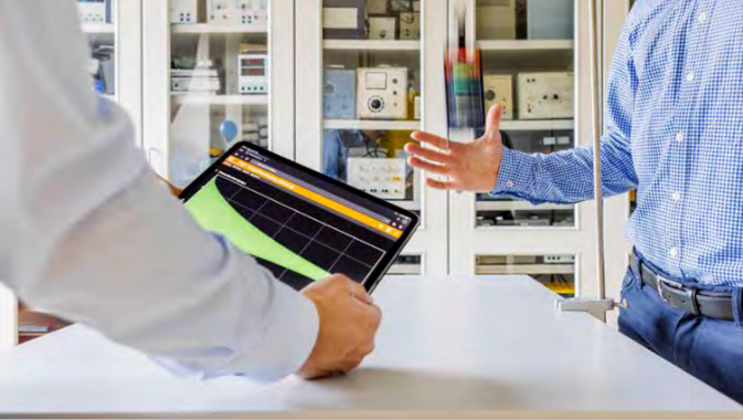 Ein gestikulierender Arm. Im Vordergrund ein weiterer Arm, der ein Tablet hält.