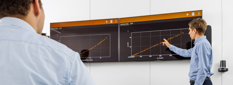 A man stands in front of two screens hanging on the wall and presents a diagram.