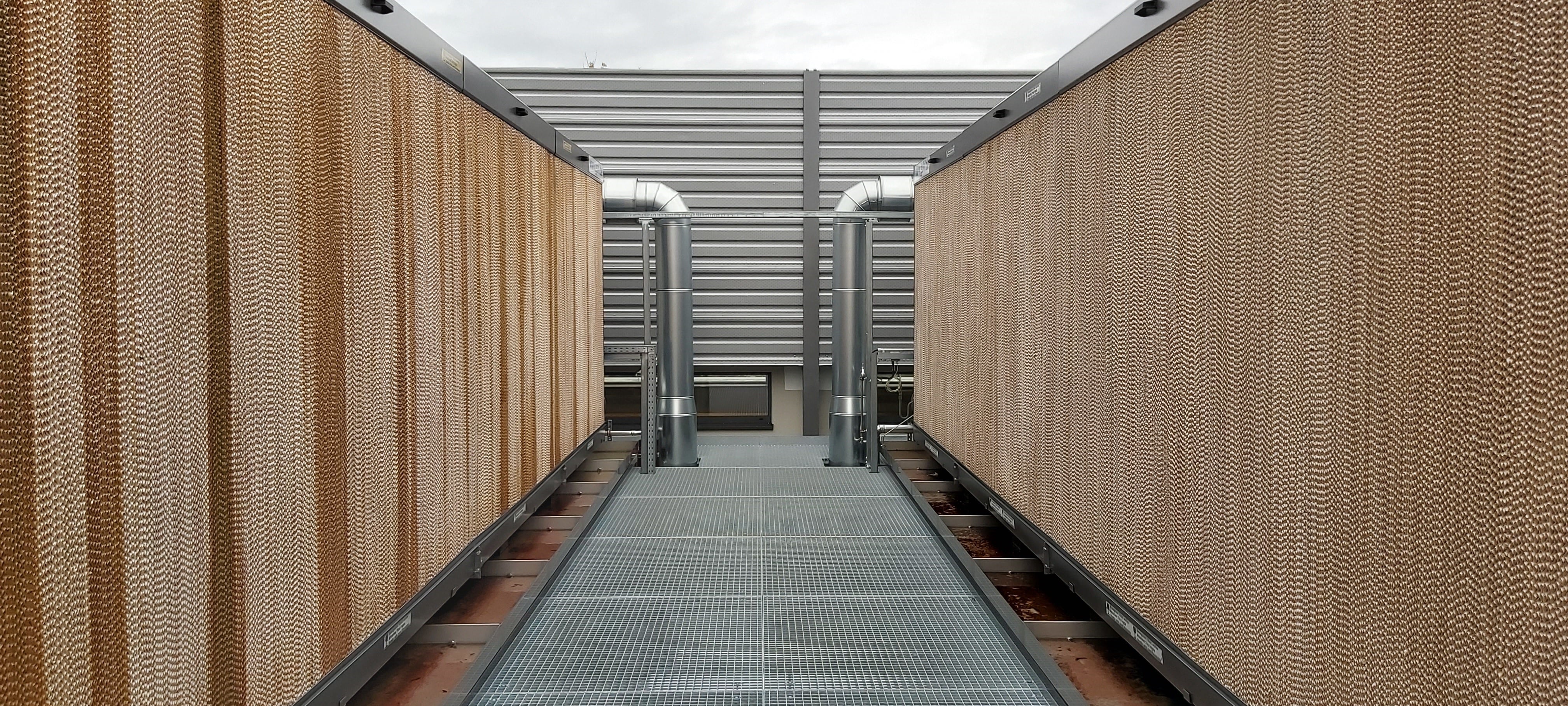 The photo shows a construction on the right and left side of a grating run. At the end, two pipes lead into the recooling unit, one on the right and one on the left. The cooling unit itself is visible from the outside with a fluted structure in light brown.